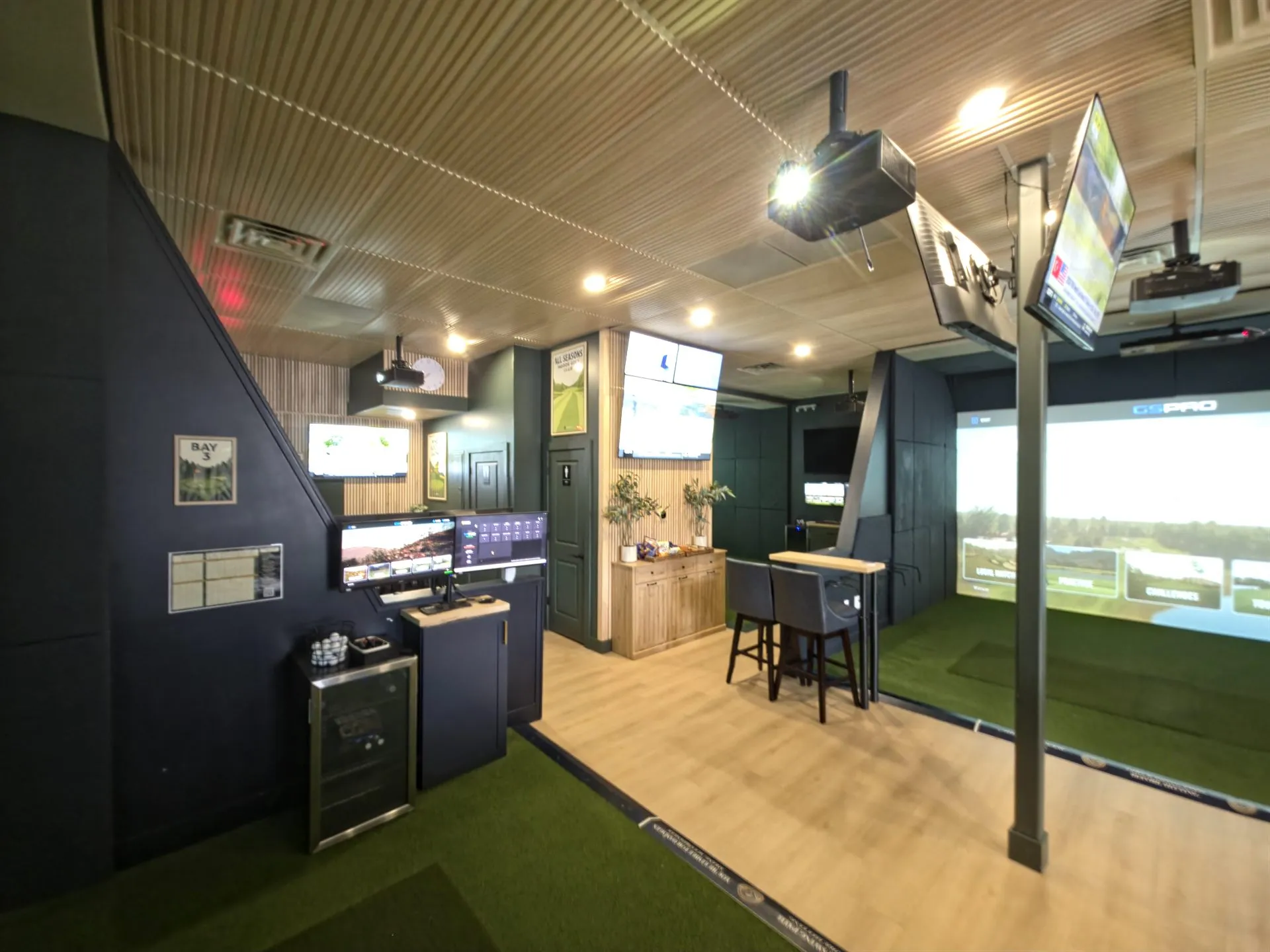 Indoor golf simulator bay with high-top bar seating and a beverage station at All Seasons, Kansas City